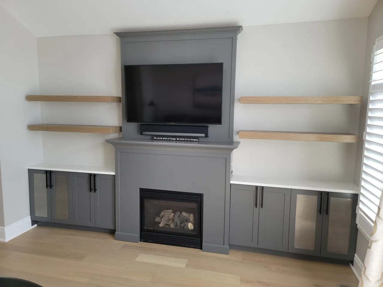 Grey built in media wall with a gas fireplace and floating oak shelves