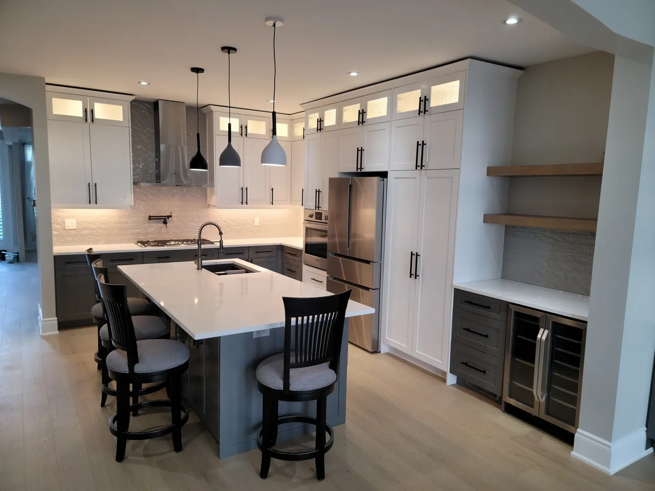Custom white shaker kitchen with a grey island, pendant lights and lit glass uppers, built by Hailey Inc in Guelph